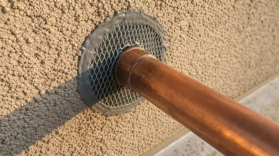 Pipe penetration in a stucco wall sealed with steel mesh and sealant during rodent proofing
